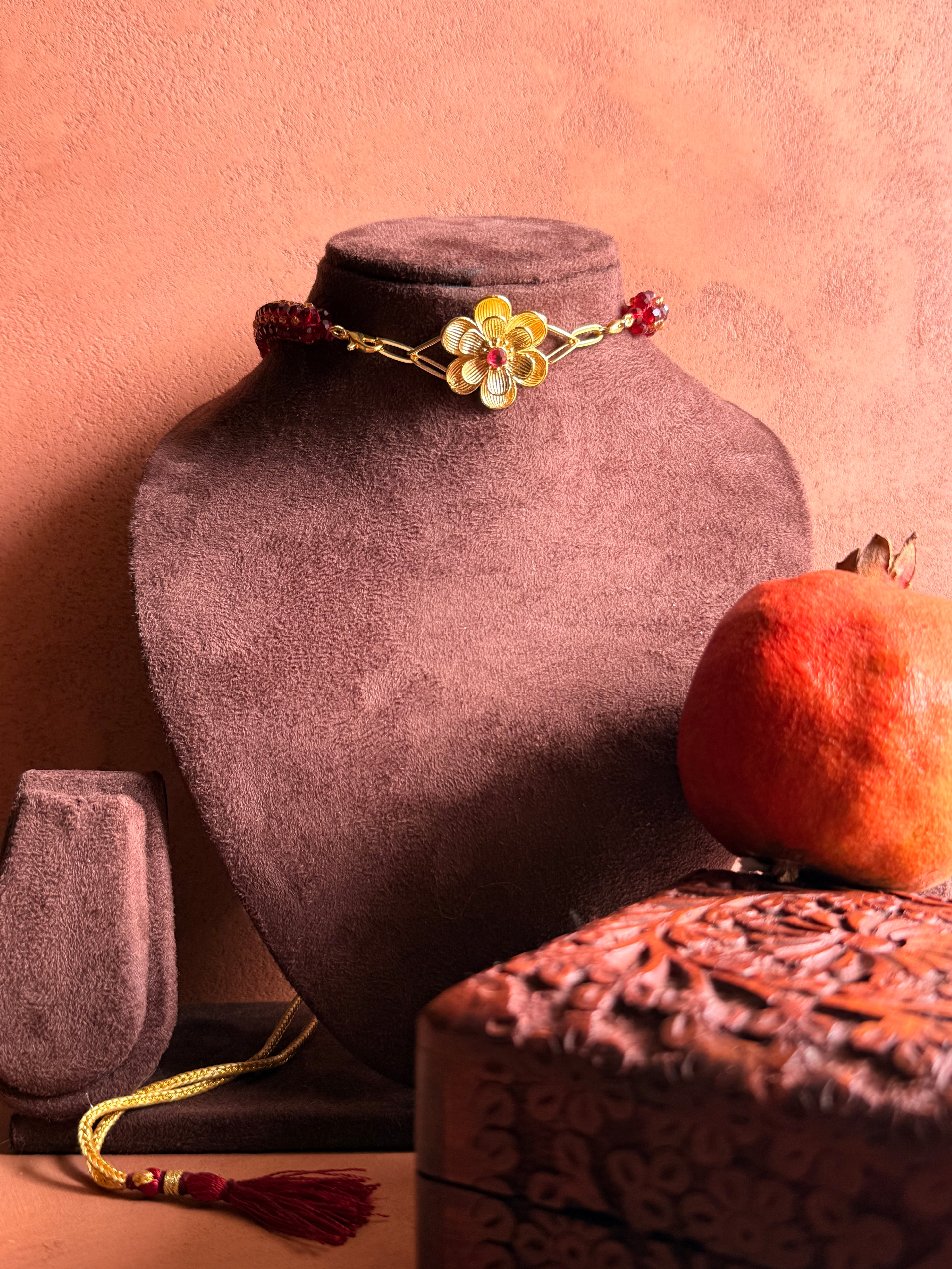 Nargis Mala garnet necklace displayed on a velvet bust, styled with a pomegranate and a carved wooden box.