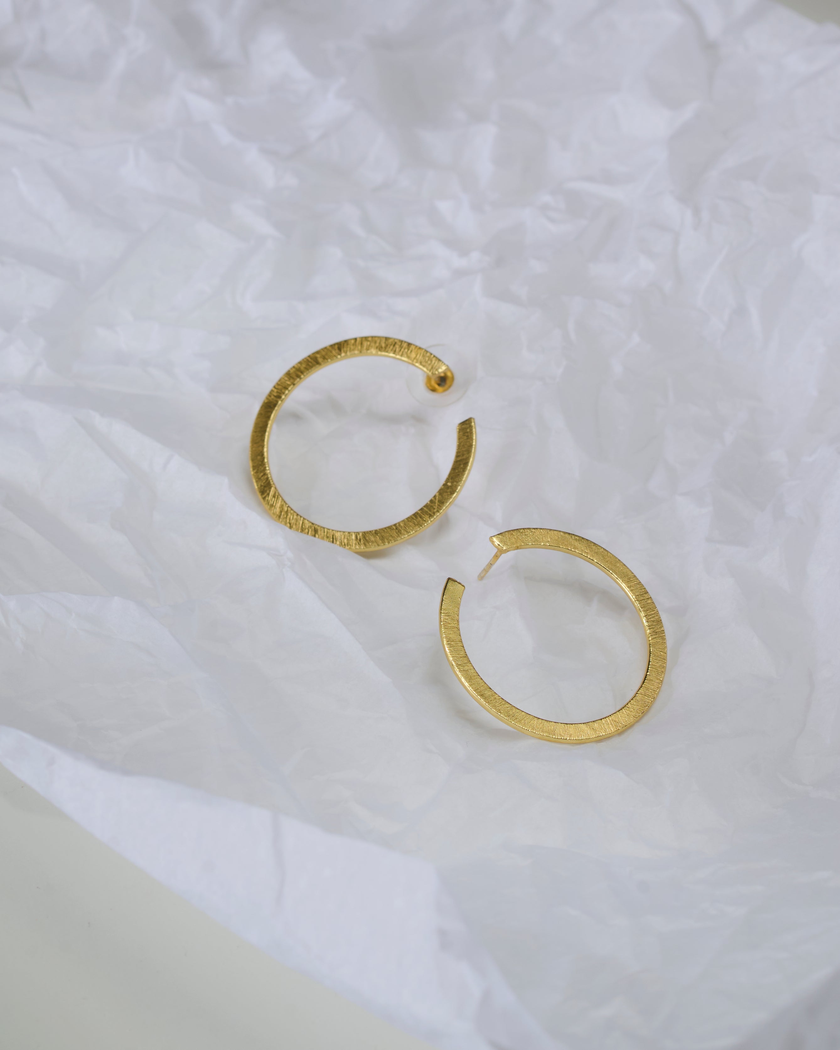 Gold toned hoop earrings on a textured white fabric background