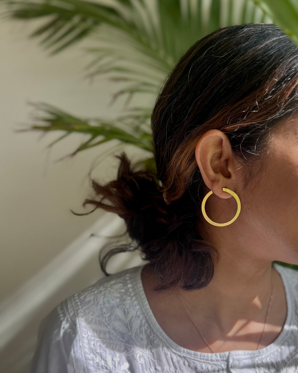 Woman wearing a gold toned hoop earring with a plant in the background