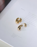 Paisley shaped gold plated double sided stud earrings kept on a book, showing front, back, open and closed views