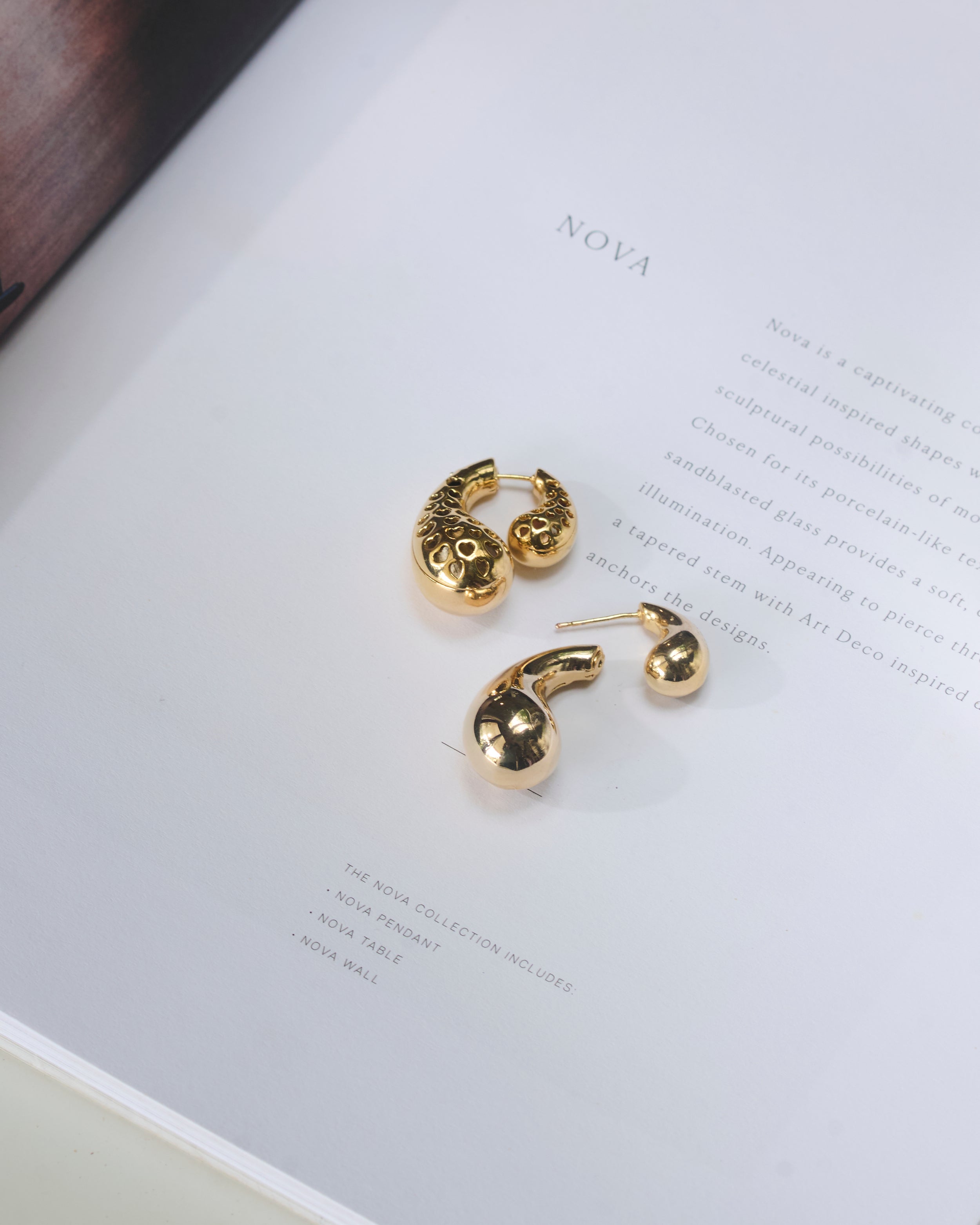 Paisley shaped gold plated double sided stud earrings kept on a book, showing front, back, open and closed views