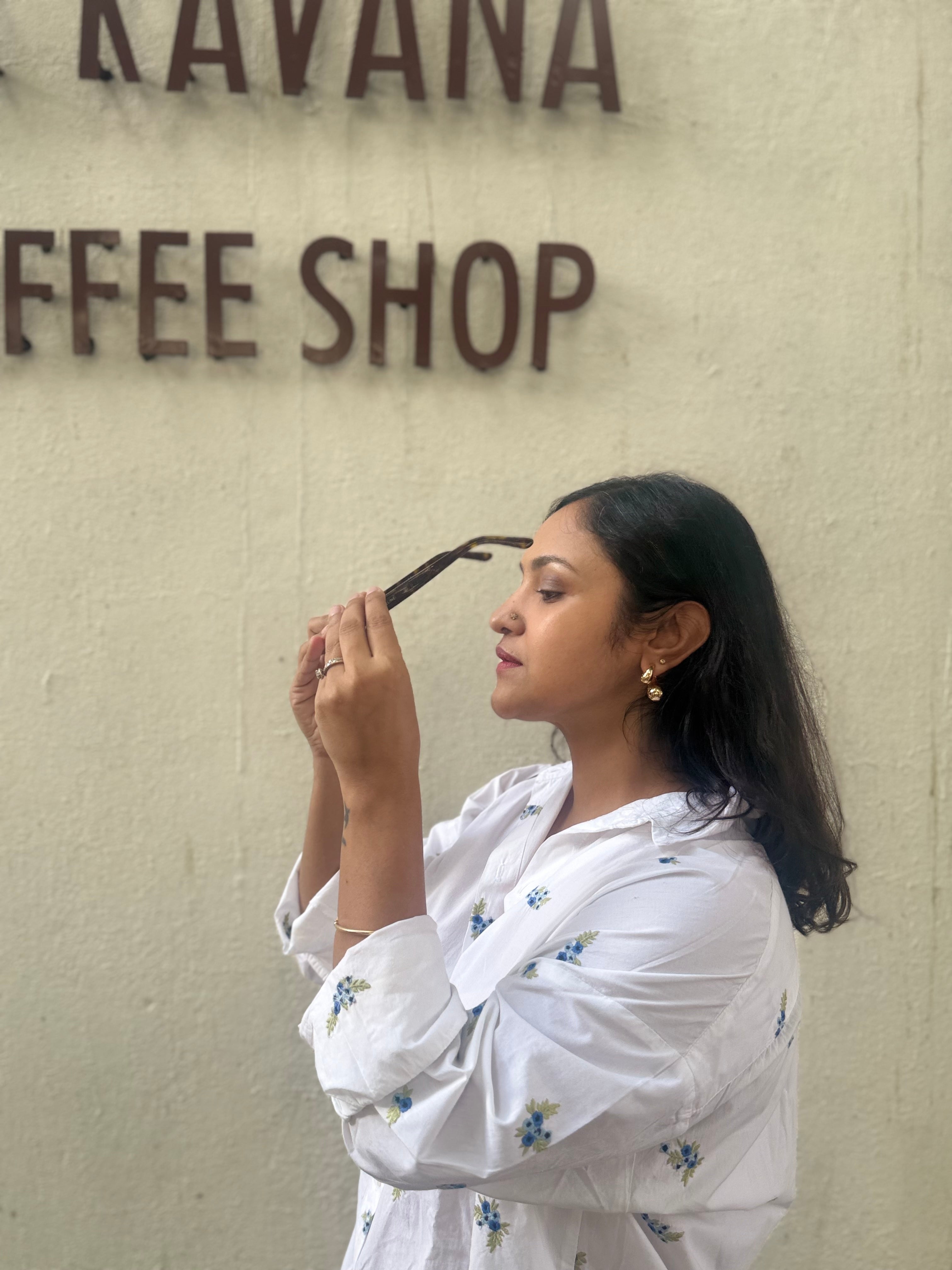 Woman holding sunglasses wearing paisley earrings in front of a Coffee Shop.