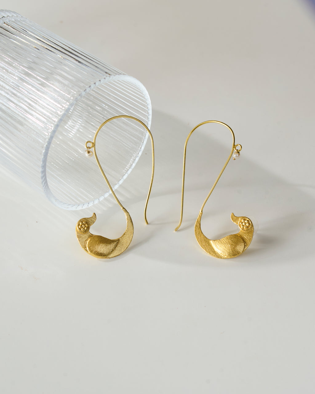 Gold plated bird shaped ear cuffs with pearl detail on a clear stand against a light gray background