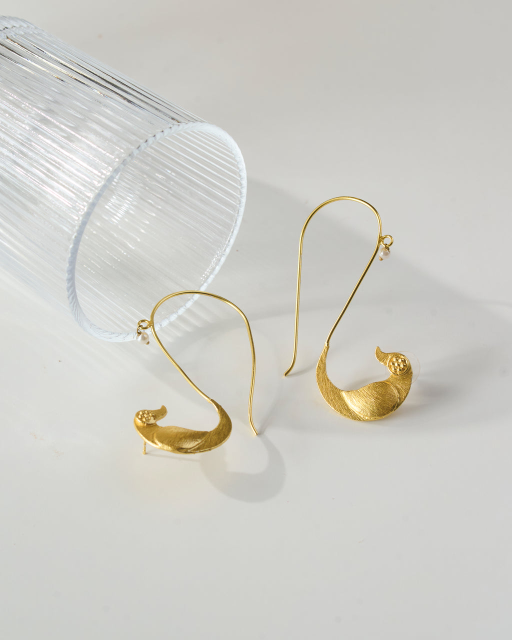 Different angle view of a Gold plated bird shaped ear cuffs with pearl detail on a clear stand against a light gray background