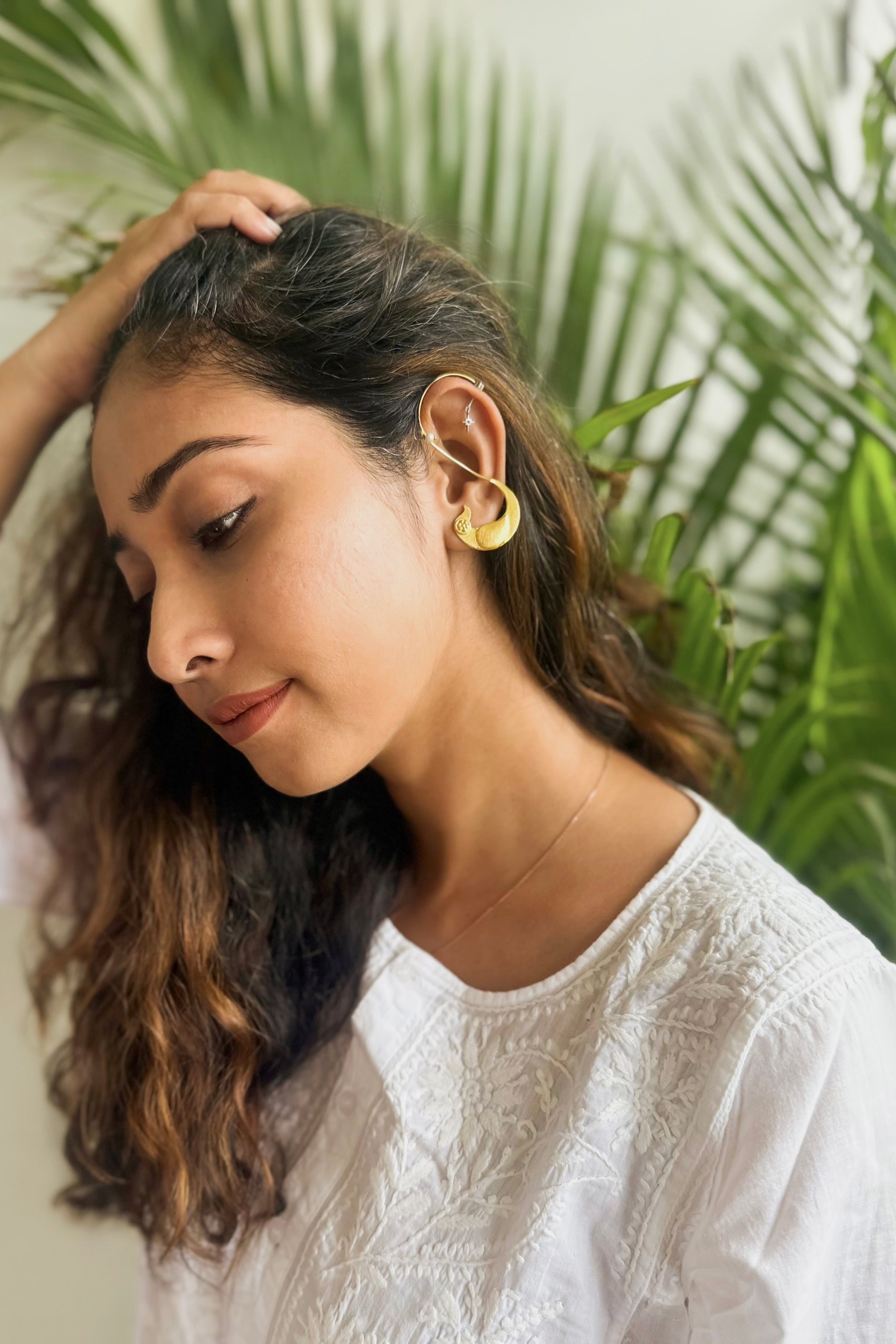 Woman wearing gold toned ear cuffs with a green leafy background