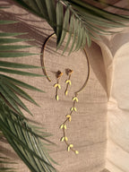 Close-up flatlay of Pallavi earrings resting against the choker, showing cascading leaf-on-chain detail, palm frond in background on linen fabric
