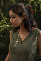 Side profile of woman wearing Pallavi set with vine shifted to side, sage green outfit, green botanical backdrop, earrings visible showing cascading leaf detail