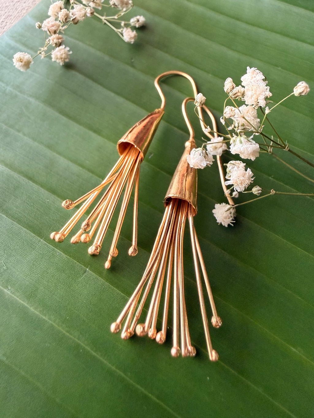 Detailed close-up shot of Parag Danglers showcasing the adjustable fine gold pollen strands against a banana leaf background.