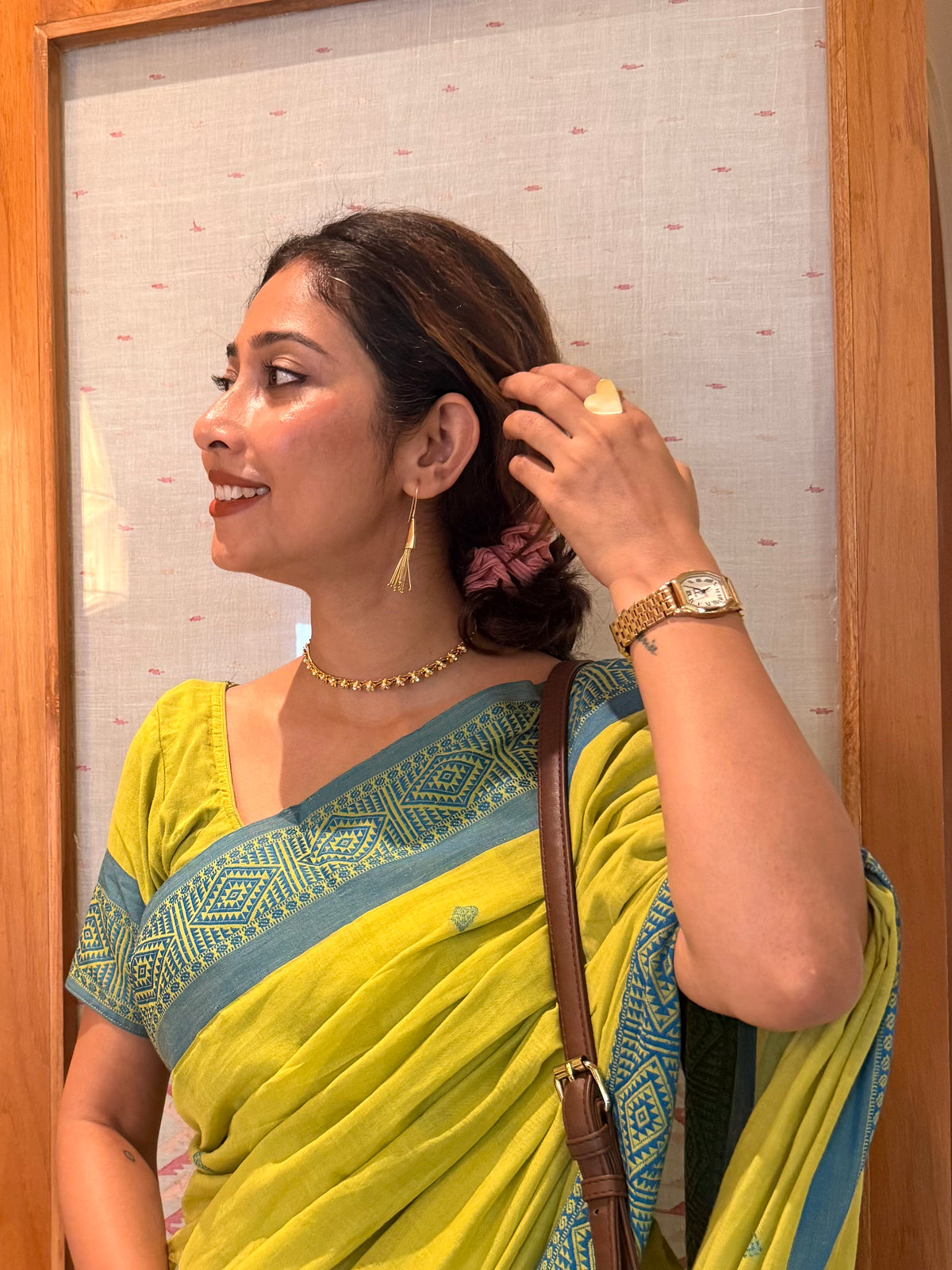 Side profile of a woman wearing gold Parag Danglers and a fine motiya choker necklace while tucking her hair back, wearing a lime green saree.