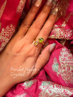 Peridot Hydro and crystal ring with a green stone beside a clear crystal point, worn on a hand resting on embroidered pink silk