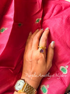 Purple Amethyst Hydro ring with a purple triangular stone on a twisted gold band, worn on a hand resting on pink silk
