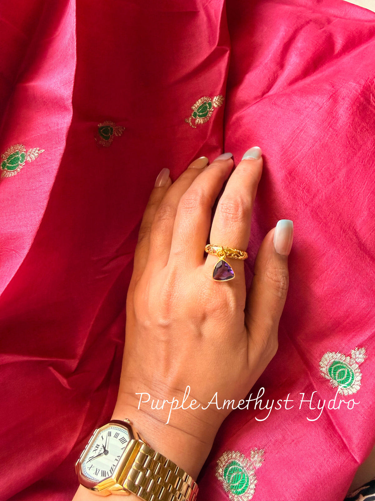 Purple Amethyst Hydro ring with a purple triangular stone on a twisted gold band, worn on a hand resting on pink silk