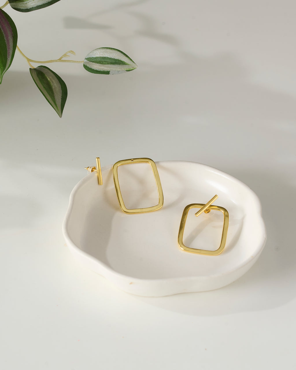 Gold plated rectangular earrings on a white dish with a light background, showing the detachable detail