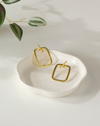Gold plated rectangular earrings on a white dish with a light background