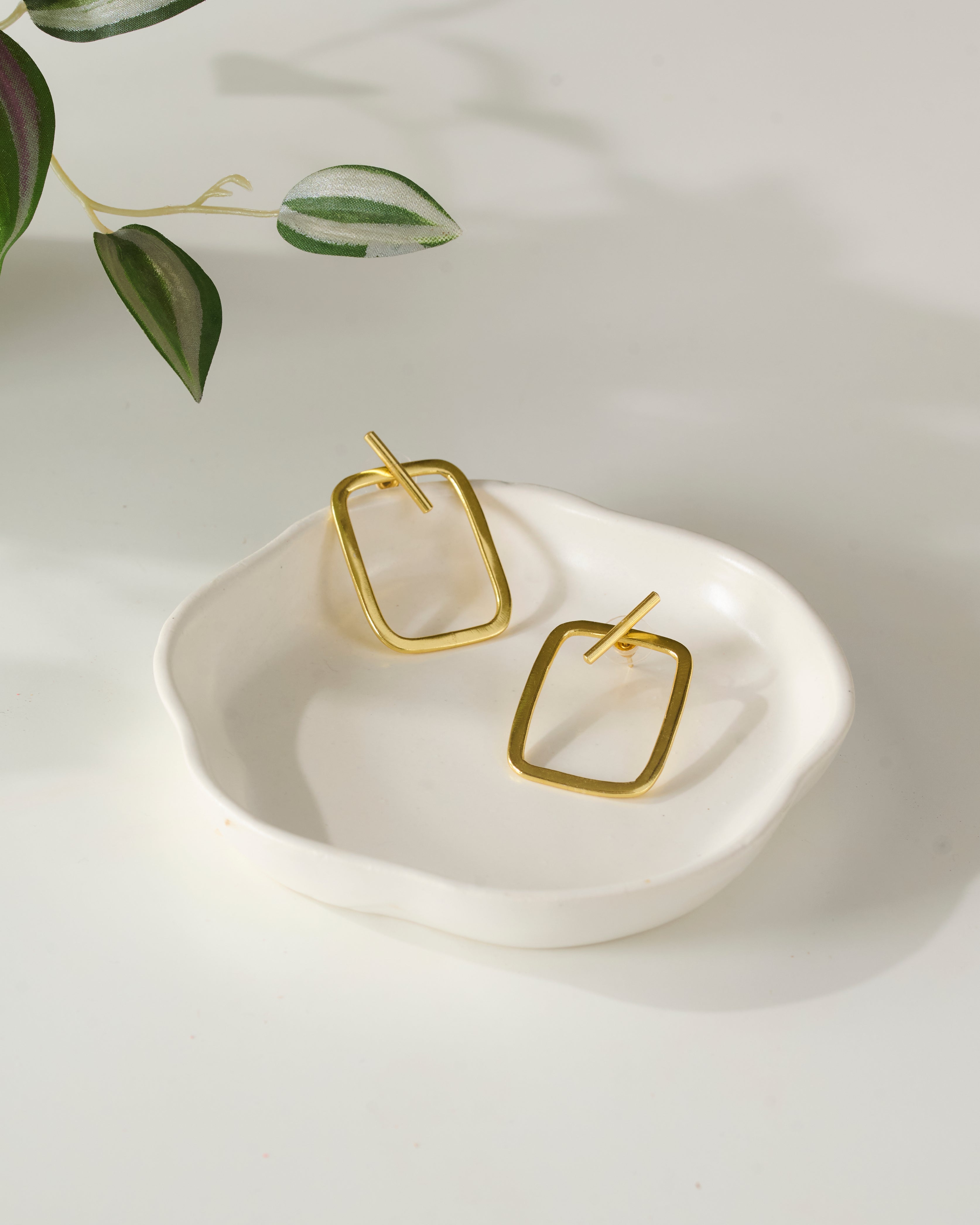Gold plated rectangular earrings on a white dish with a light background