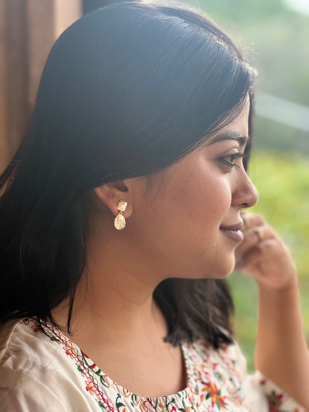 Woman wearing gold toned earrings with a blurred natural background