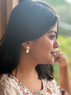 Woman wearing gold toned earrings with a blurred natural background