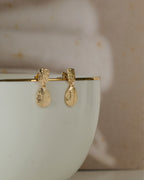 Close up of Small textured gold toned earrings with rain drop shape danglers kept on a white mug.