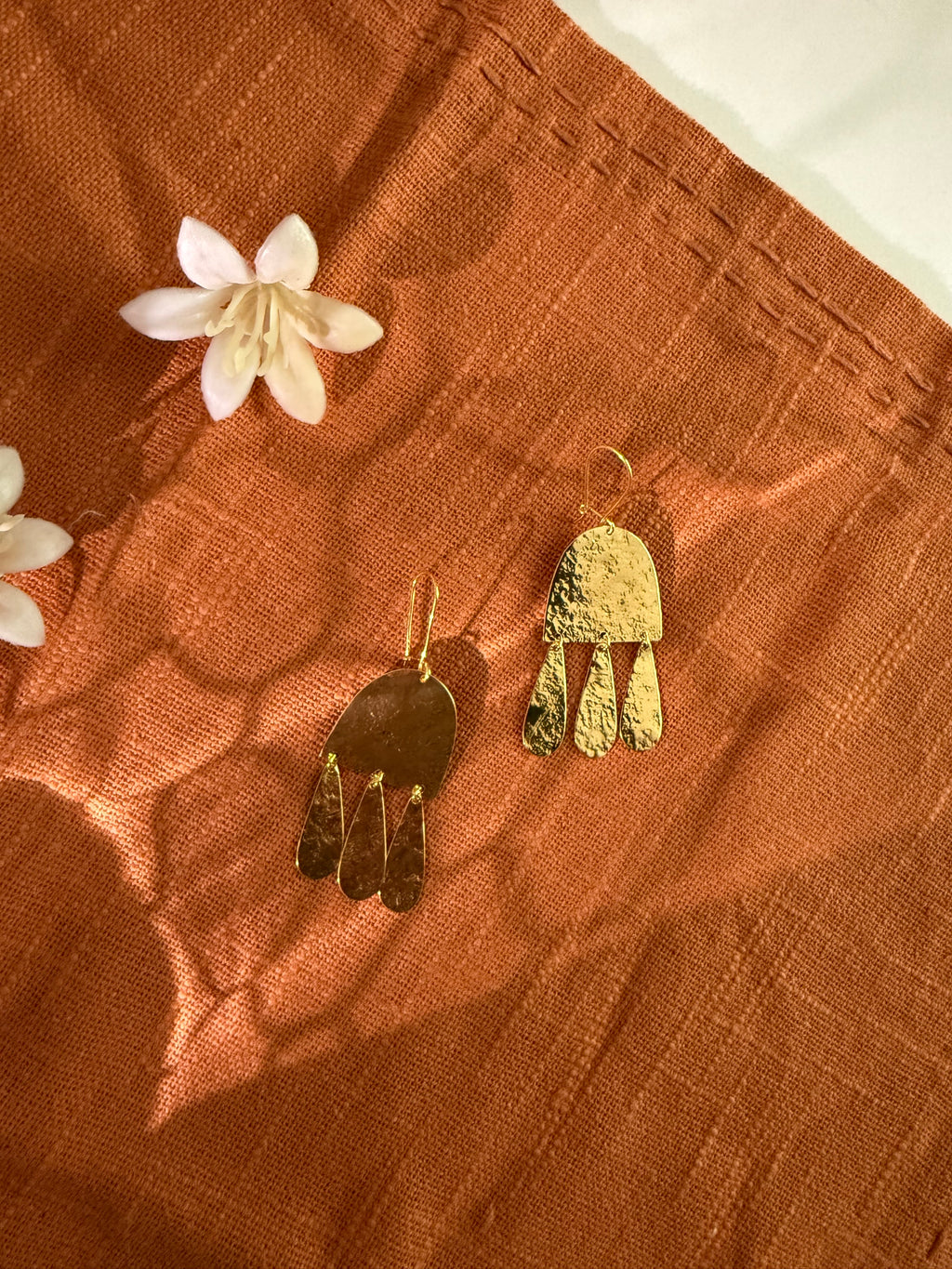 Gold earrings on a textured brown surface with white flowers with glowing light effect.