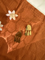 Gold earrings on a textured brown surface with white flowers with glowing light effect.
