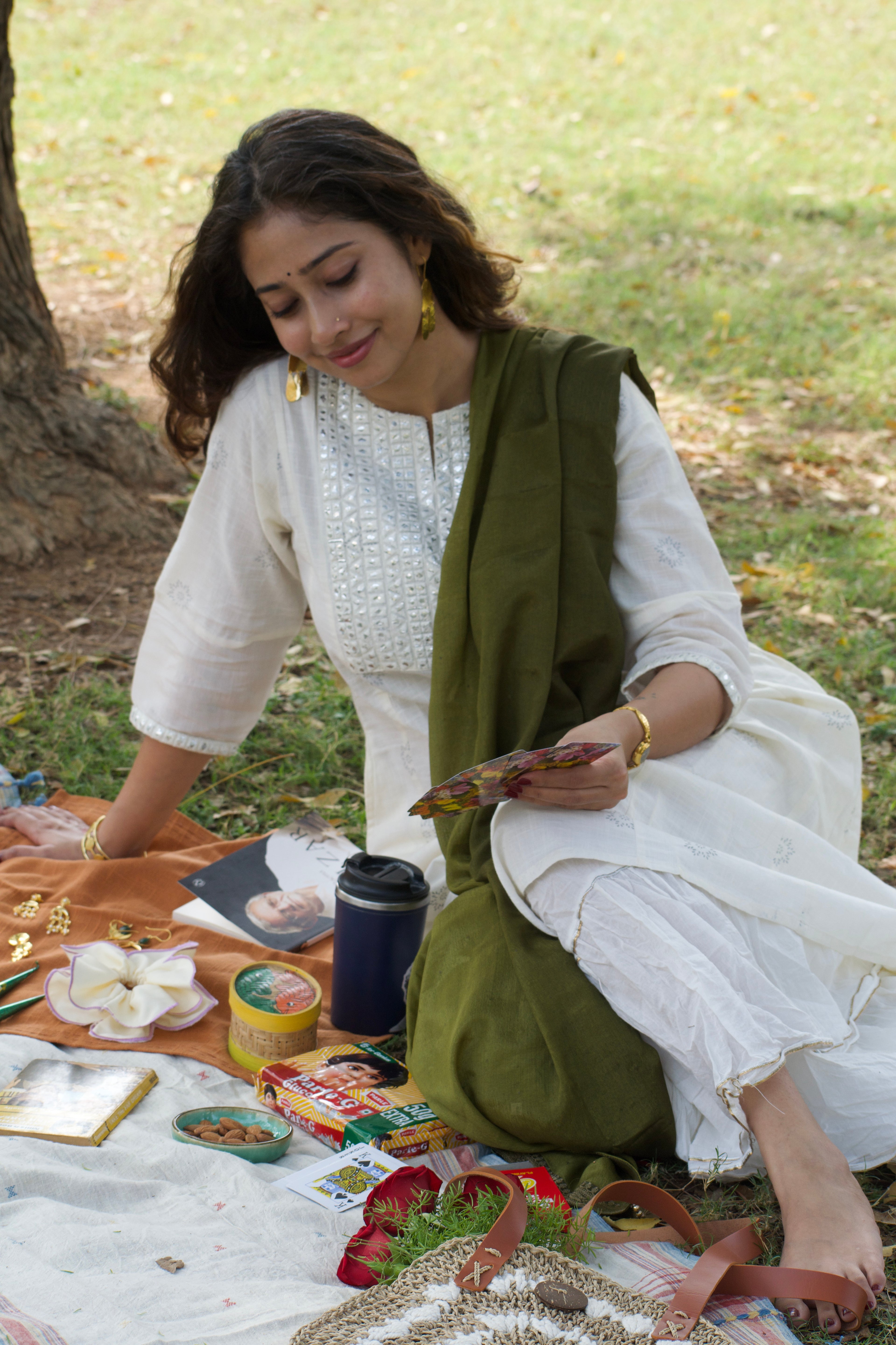 Woman sitting outdoors with a picnic blanket and food items, wearing saanjh danglers