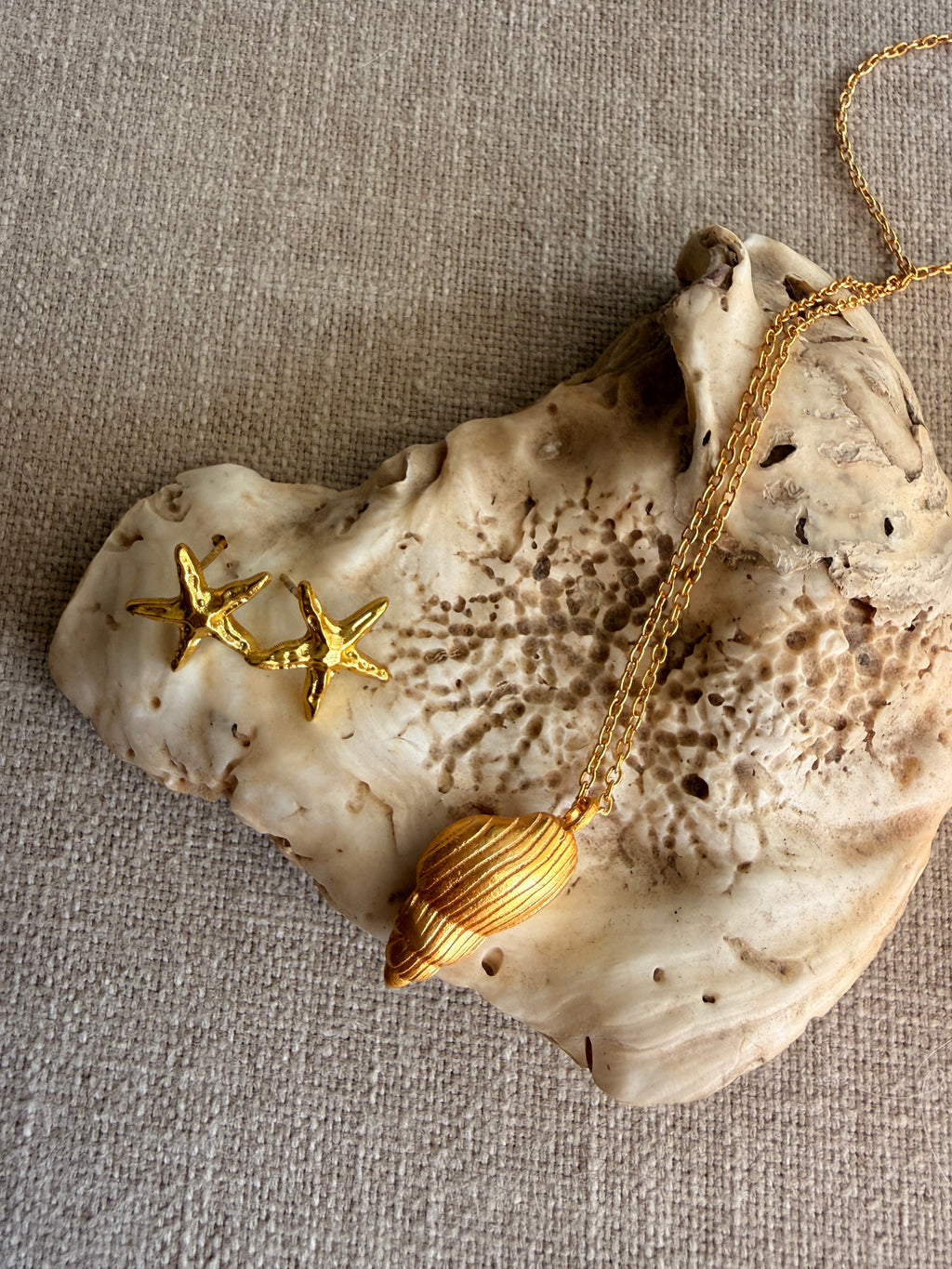 The Sagarika shell pendant necklace styled alongside the gold starfish Sagar Studs on a textured piece of natural shell.