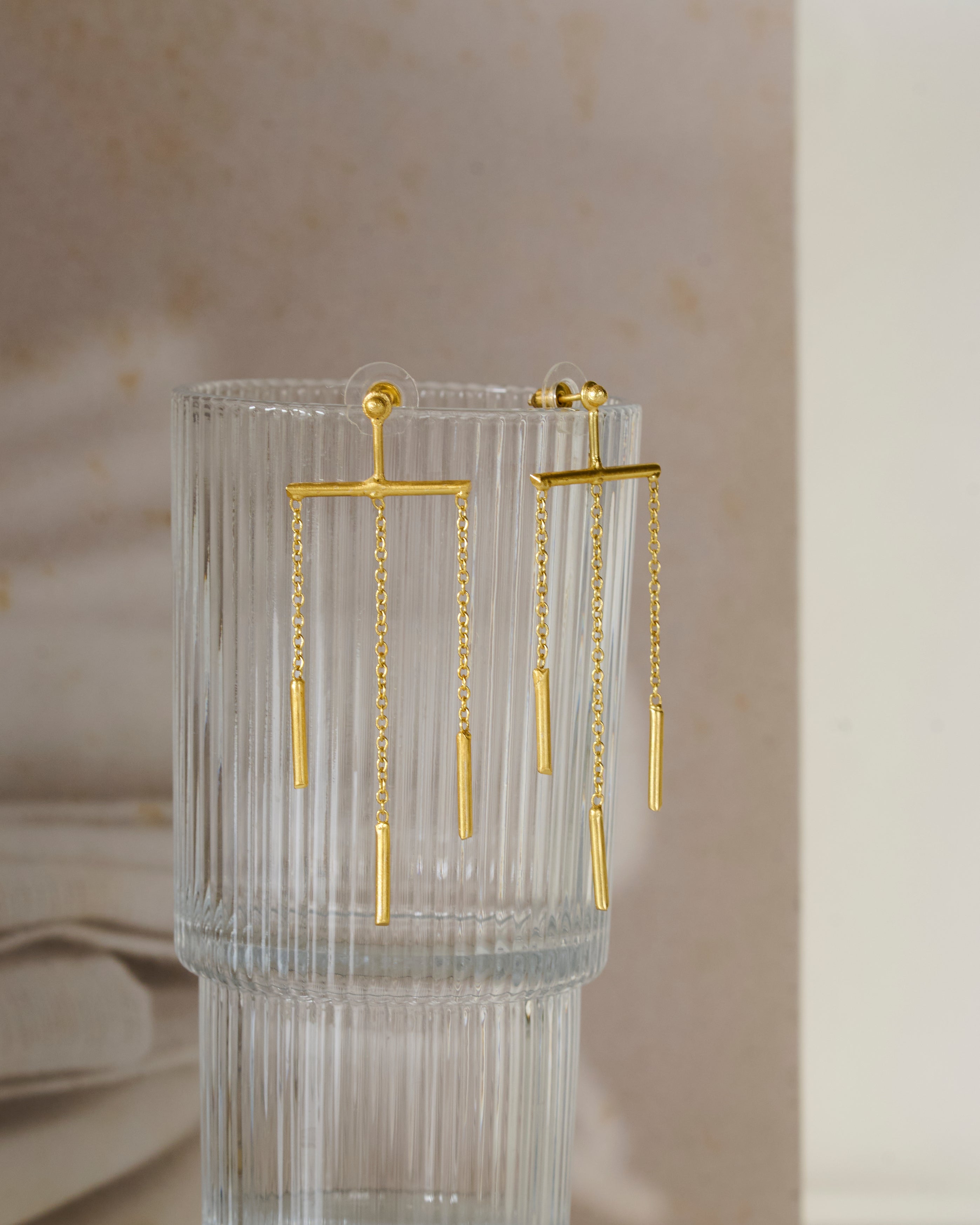 Fluted glass vase with gold toned chain dangling earrings on neutral background.