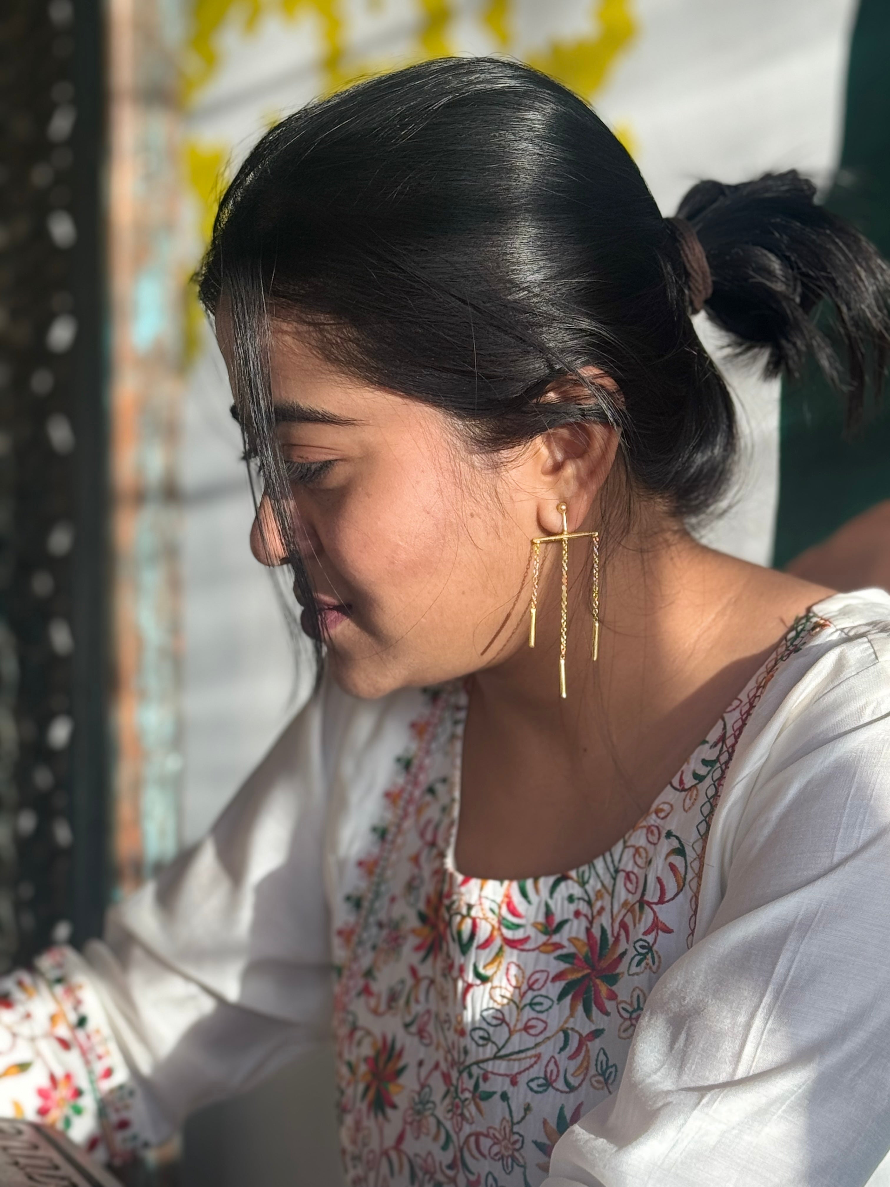 Woman wearing a floral white kurta with gold toned dangling earrings, with sun on her face. 