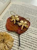 Close up of gold plated four-leaf clover earrings on a red pressed flower, kept on an open book.