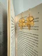 Gold plated four-leaf clover earrings on an open book
