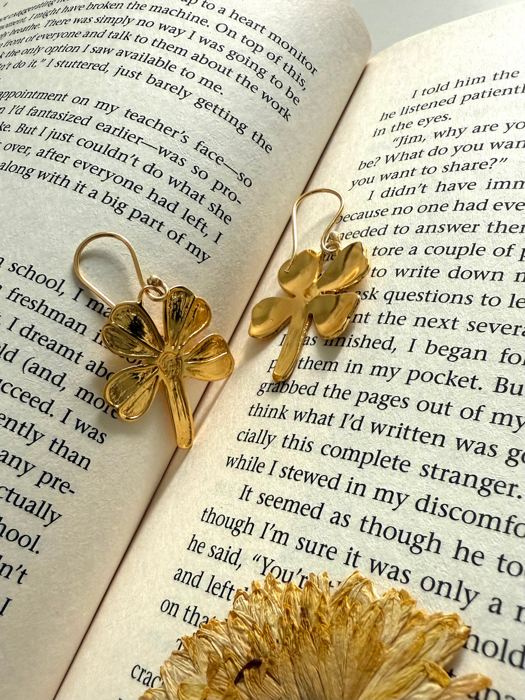 Gold plated four-leaf clover earrings on an open book, back and front visible.
