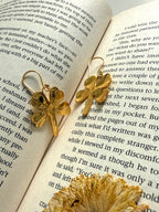 Gold plated four-leaf clover earrings on an open book, back and front visible.