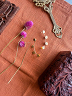 Sitara ear cuffs flatlay on terracotta linen showing both cuffs separated, styled with dried pink and purple flowers, carved wooden box and antique mirror handle in background