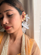 Close-up of woman wearing Sitara ear cuffs with white flowers in hair, eyes cast downward, dressed in a warm golden outfit, soft indoor light