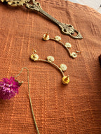 Close-up flatlay of Sitara ear cuffs back side on terracotta fabric, coin disc detail clearly visible, dried purple Globe Amaranth flower beside them