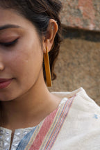 Close-up of a woman wearing a gold earring with a blurred background, half face visible.