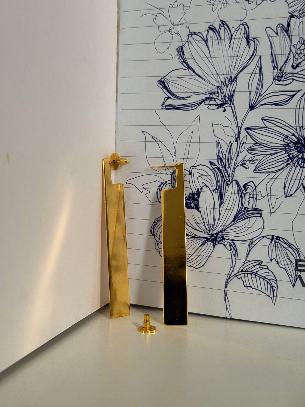Gold plated geometric dangler ear studs on a notebook with hand drawn floral design.
