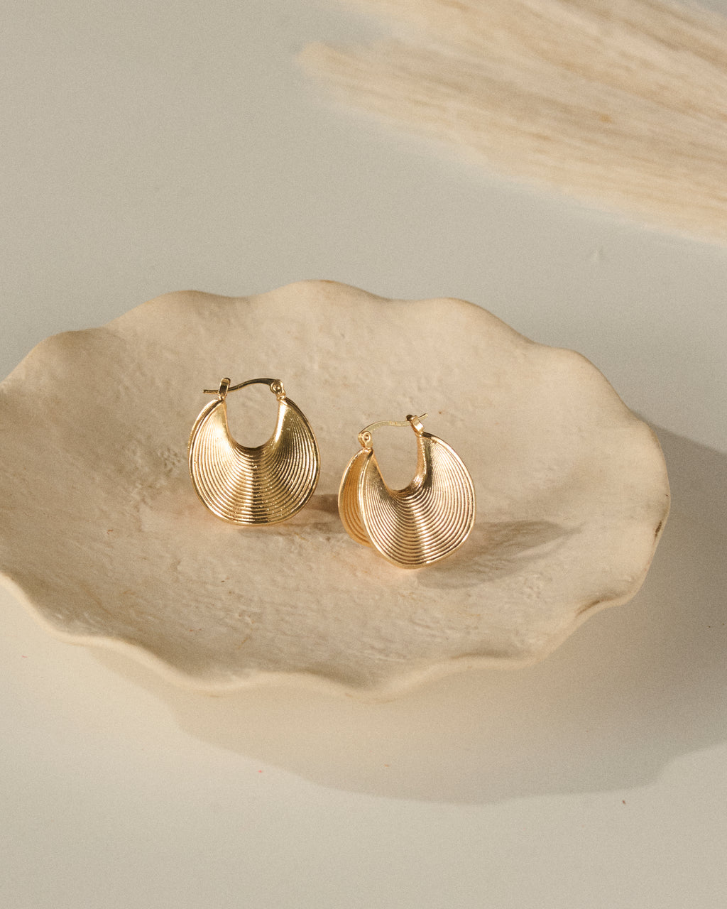 Gold hoop earrings with ripple effect design on a textured beige plate with scallops