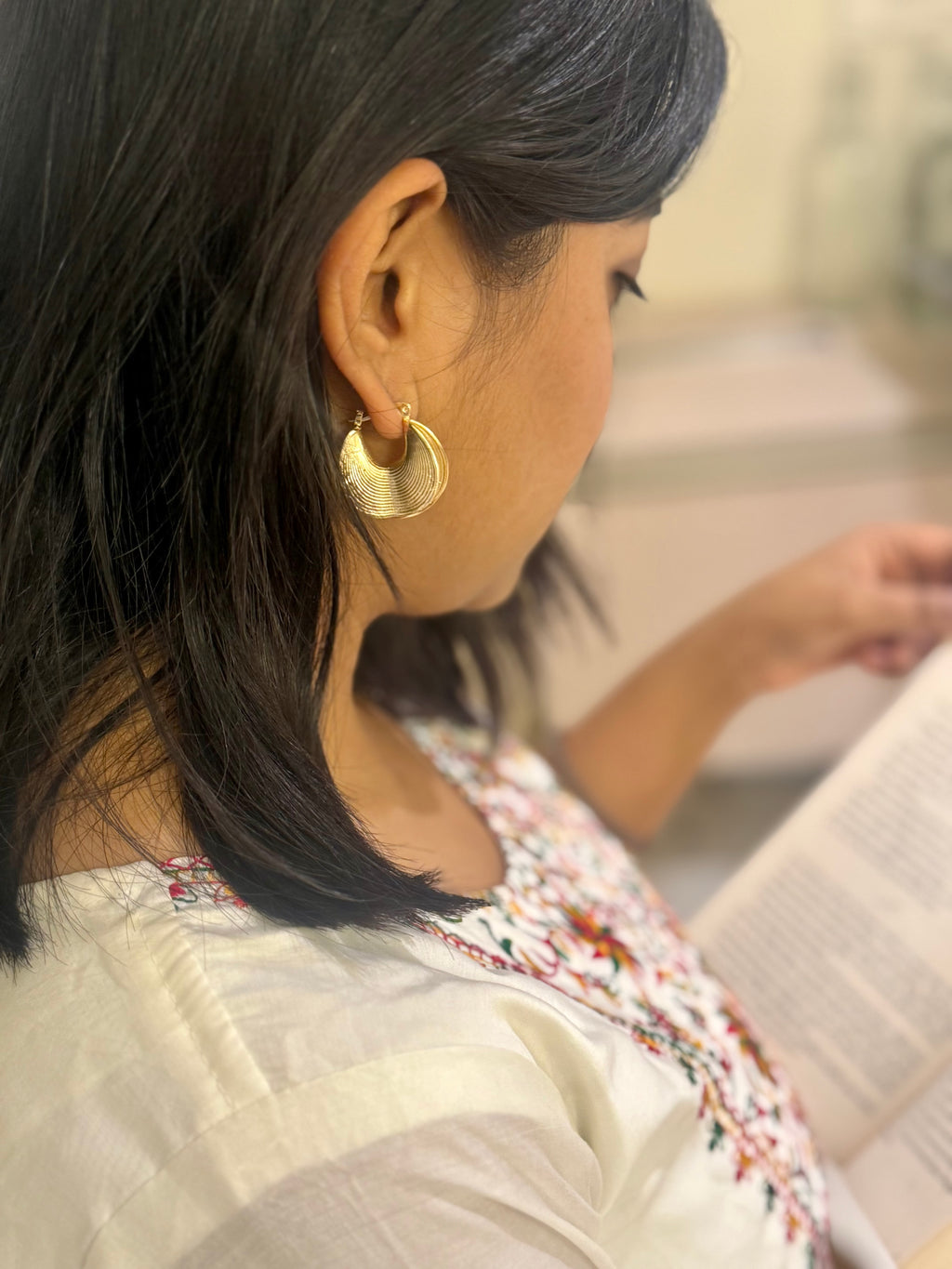 Woman wearing gold hoop earrings, looking at a book.