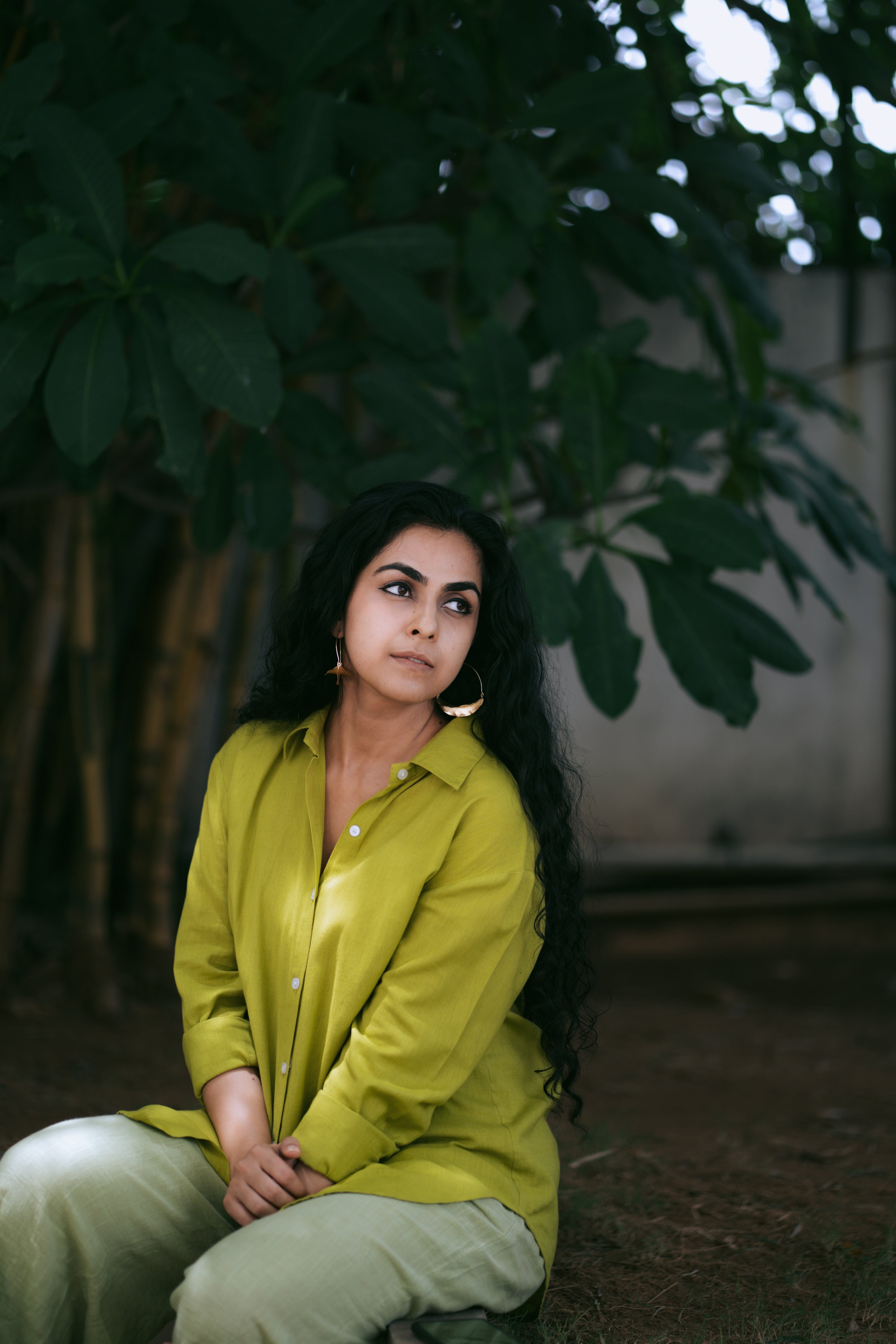 Woman in a green outfit sitting outdoors with greenery in the background, wearing Tarang Leaf Hoops.