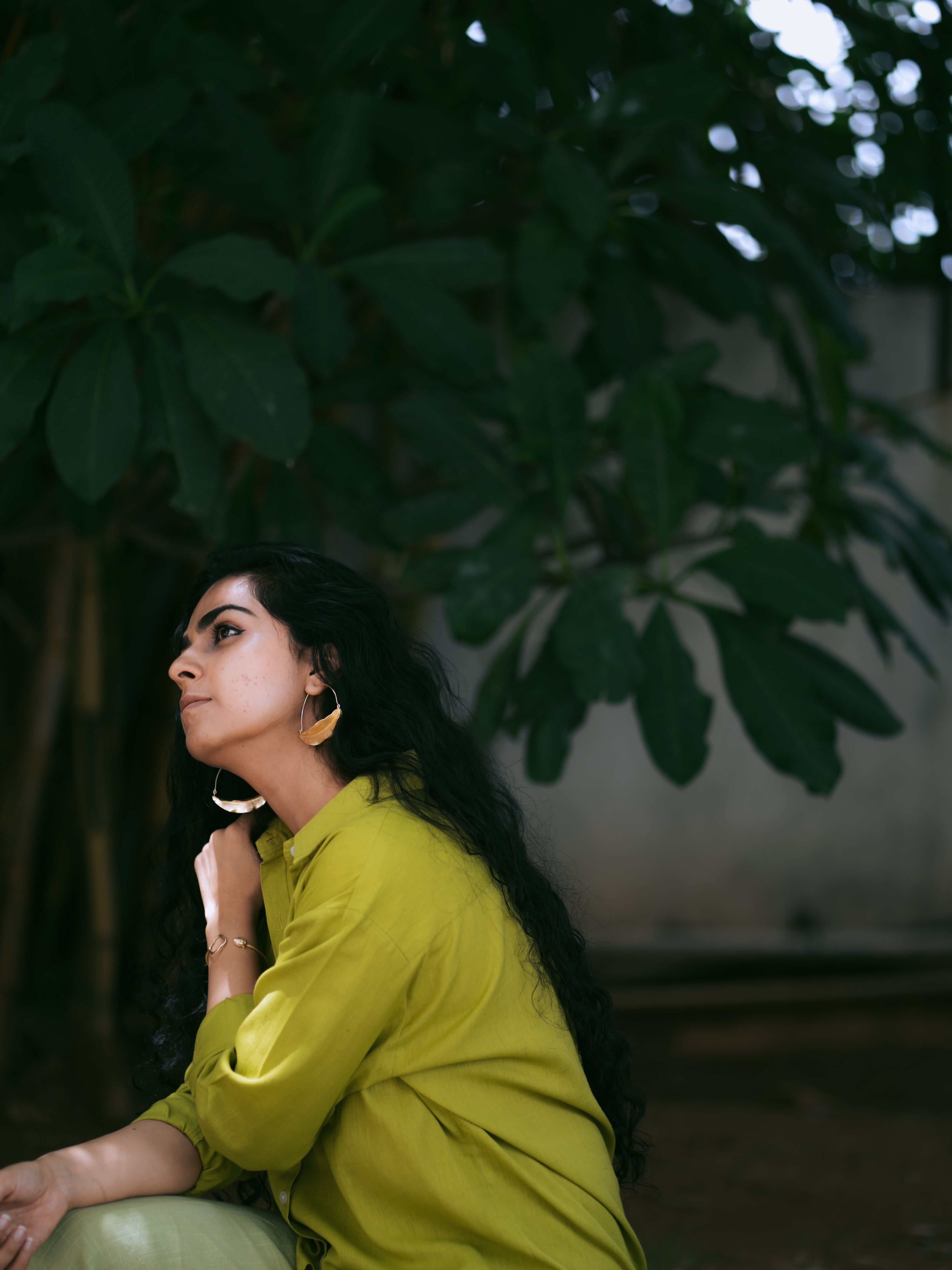 Woman in a green outfit sitting outdoors with greenery in the background, wearing Tarang Leaf Hoops