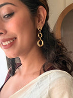 Close-up of a smiling woman in a white saree wearing a Valaya Dangler, three linked hammered gold rings