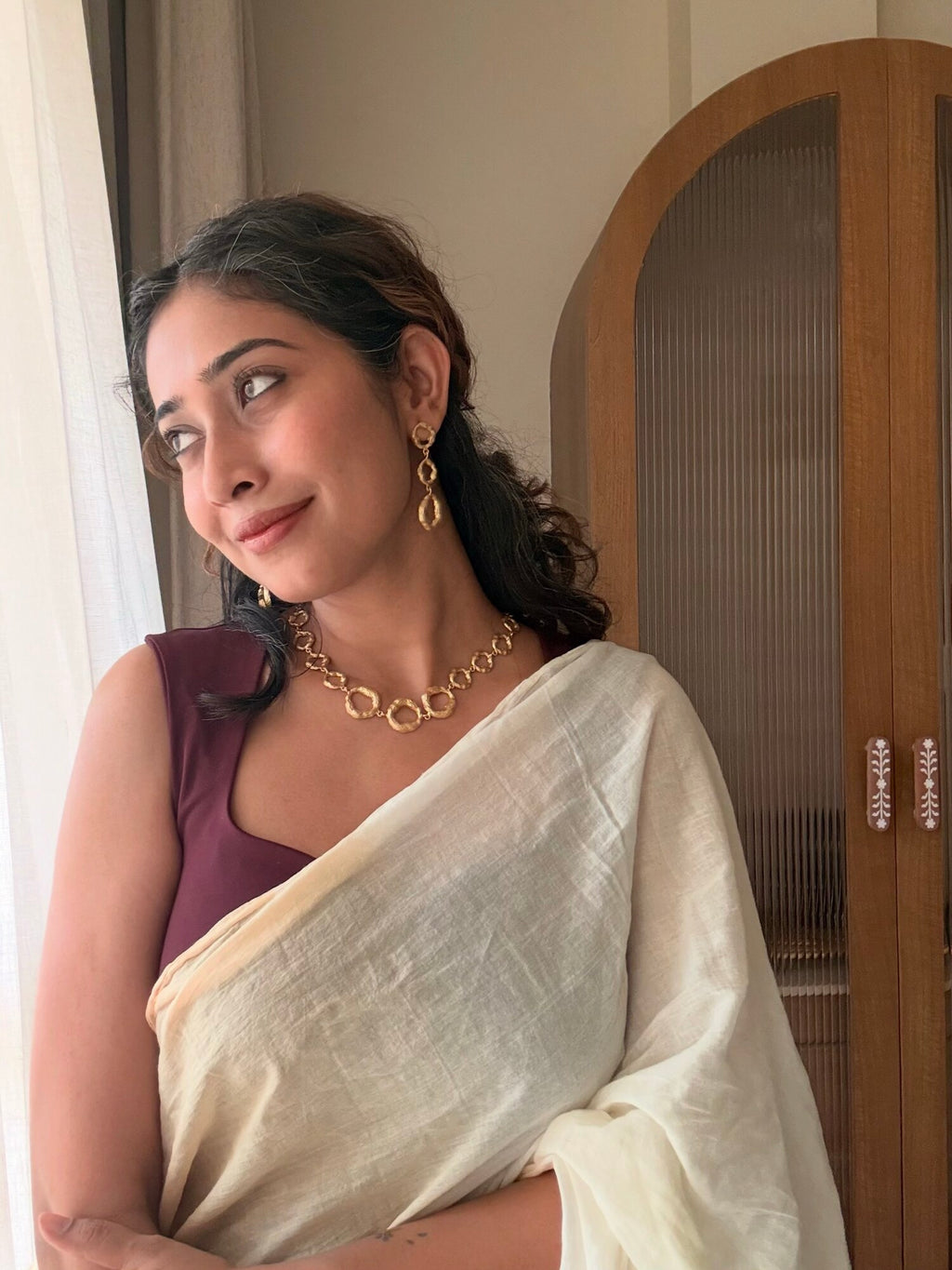 Woman in a white saree and maroon blouse looking out a window, wearing Valaya Danglers with the Valaya Necklace
