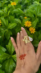 Hand wearing a floral ring with yellow flowers and green leaves in the background
