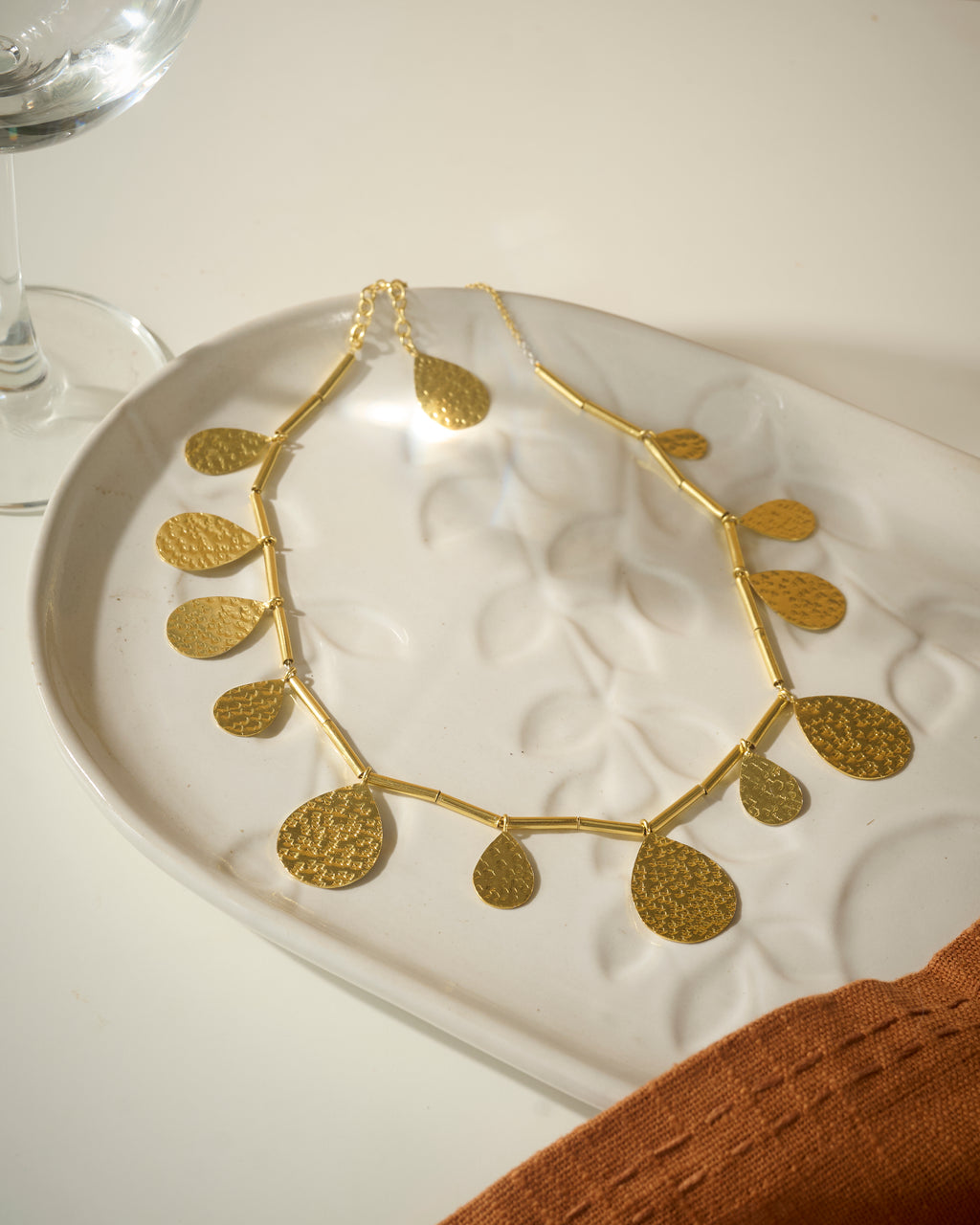 Gold plated necklace with big drops pendants kept on a organic textured while plate.