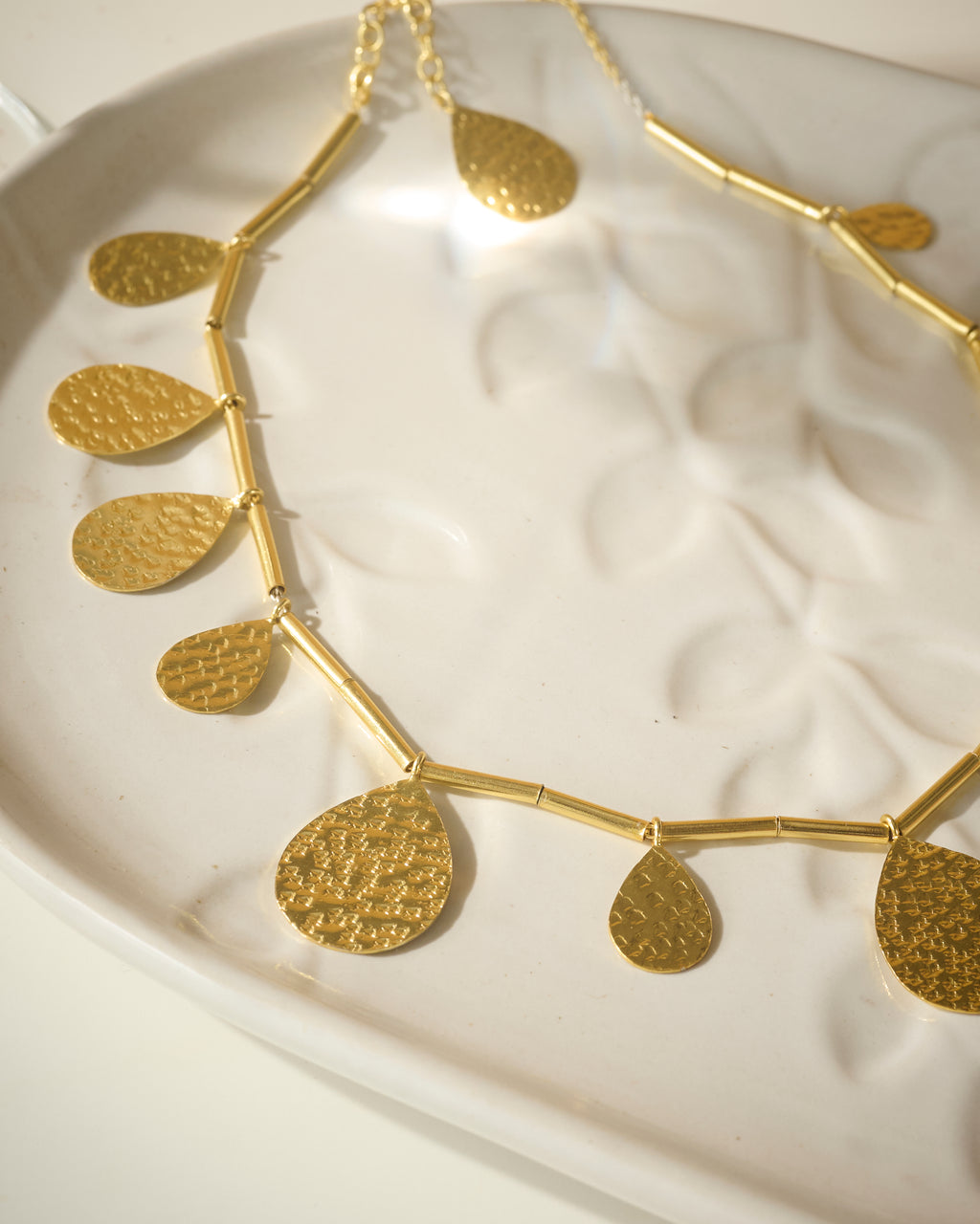 Closeup of Gold plated necklace with big drops pendants kept on a organic textured while plate.