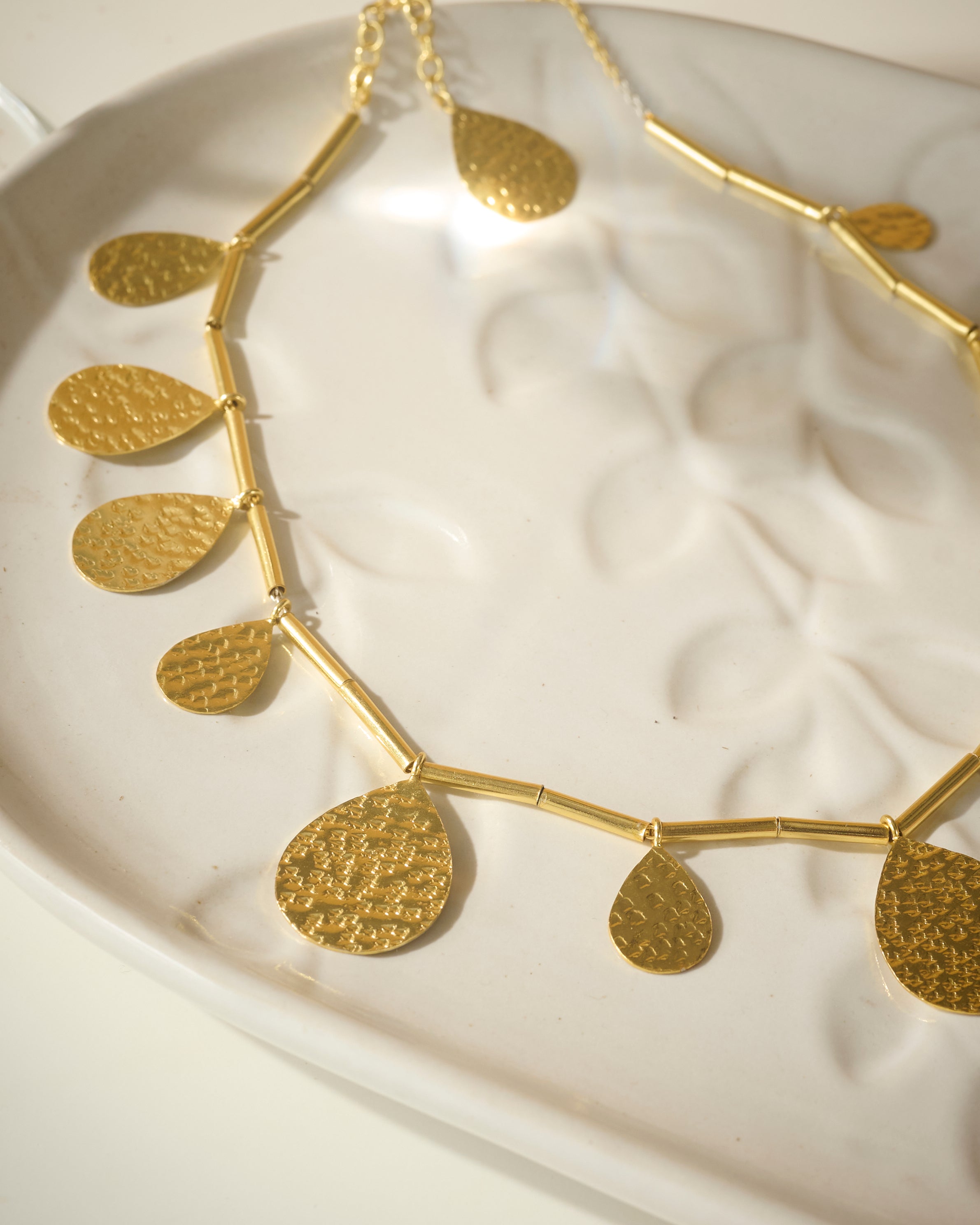 Closeup of Gold plated necklace with big drops pendants kept on a organic textured while plate.